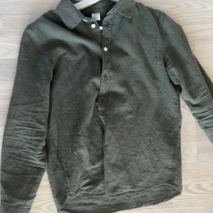 Grön linneskjorta från Lindex - Snygg grön skjorta i linne från Lindex. Skjortan har klassisk krage, långa ärmar och knäppning framtill med vita knappar. Perfekt för en stilren och avslappnad look.