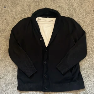 Svart kofta  - Säljer en stilren svart kofta från H&M. Den har långa ärmar och knappar framtill. Perfekt för att hålla sig varm och snygg under kyligare dagar.Size L