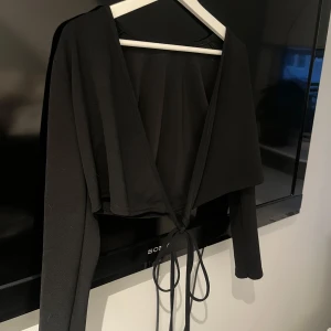 Svart omlottopp med långa ärmar från Missay - Säljer en svart omlottopp från Missay med långa ärmar och knytband i midjan. Toppen har en v-ringad design och är i ett mjukt, stretchigt material. Perfekt att styla till olika outfits!