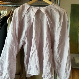 Ljuslila blus i linnetyg - Säljer en ljuslila blus med långa ballongärmar och lös passform. Blusen är tillverkad i linne med veckdetaljer framtill. Blusen är från Lindex.
