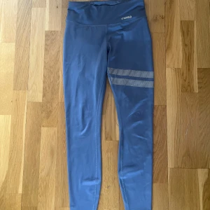 Blå träningstights från Stronger - Snygga blåträningstights från Stronger med två vita prickiga ränder på ena benet. Hög midja och stretchigt material som sitter tight men bekvämt. Använt mycket och har en fläck på baksidan som ej går bort men inget man tänker på. Några prickar har gått bort på insidan av låret💘
