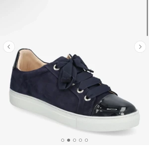 Mörkblå sneakers med lackad tå och breda snören - Snygga mörkblå sneakers med breda snören och lackad svart tå. Skorna har vit platt sula och silverfärgade öljetter. Perfekta för en trendig och avslappnad stil.