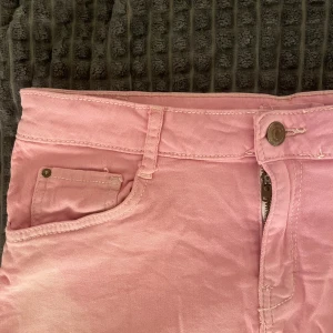 Rosa jeanskjol från Gina Tricot - Säljer en ljusrosa jeanskjol från Gina Tricot med rå kant nertill och klassiska femficksdetaljer. Kjolen har knapp och dragkedja framtill samt bälteshällor i midjan. Perfekt för dig som gillar färg och denim.