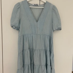 Ljusblå kortklänning med v-ringning från Zara - Supersöt ljusblå klänning från Zara med v-ringning och puffärmar. Klänningen har volanger i kjolen och är tillverkad i ett mjukt bomullsliknande material. Perfekt för vår och sommar!