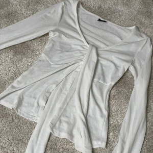 Vit omlottopp med knyt  - Säljer en vit långärmad omlottopp från Gina Tricot i mjukt material. Toppen har v-ringning och långa band framtill som kan knytas i midjan för en snygg look. Är XXS men passar även XS