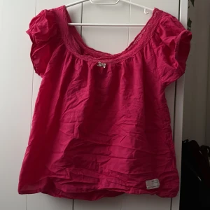 Ceriserosa blus från Odd Molly - Säljer en jättesöt ceriserosa blus från Odd Molly med korta puffärmar och bred, virkad kant vid halsringningen. Blusen har broderad detalj på ryggen och är tillverkad i ett lätt och luftigt material. Perfekt för vår och sommar! Passar storlek XS/S