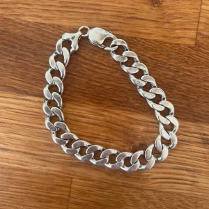 Silverfärgat kedjearmband - Säljer ett chunky armband i silverfärgad metall med breda, platta länkar. Armbandet har ett klassiskt karbinlås och mäter cirka 21 cm långt. Perfekt för dig som gillar statement-smycken och vill addera lite edge till din stil.