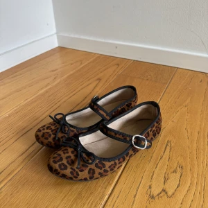 Leopardmönstrade ballerinaskor - Säljer ett par ballerinaskor med leopardmönster, svarta detaljer och söt rosett framtill. Skorna har en rem med spänne över foten för extra stil och passform. Ens sulan är lite smutsig men annars inga tydliga defekter 