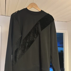 Svart sweatshirt med sammetsdetalj från La Vichy - Säljer en svart sweatshirt från La Vichy i storlek S. Tröjan har en unik diagonal sammetsdetalj på framsidan som ger en cool look. Klassisk rund halsringning och långa ärmar. Perfekt för dig som vill ha något stilrent men ändå speciellt.