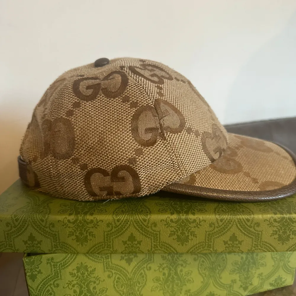 Snygg beige keps från Gucci med klassiskt GG-mönster i brunt. Kepsen har böjd skärm och är tillverkad i bomullsmaterial med detaljer i brunt runt skärmen. Perfekt accessoar för en trendig look.. Asusteet.