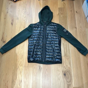 Svart och mörkgrön hybrid från Peak Performance - Snygg hybrid från Peak Performancemed glansig svart pufferfront och mörkgröna ärmar och rygg. Storlek L men passar till M. Köpt för 1800+ men säljer för 750
