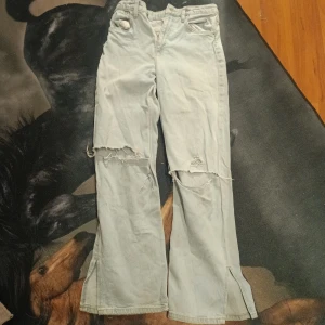 Ljusblå vida jeans från H&M - Ljusblå jeans från H&M med hög midja och vida ben. Byxorna har slitna detaljer och hål vid knäna samt slitsar nertill. Perfekta för en avslappnad och trendig look.