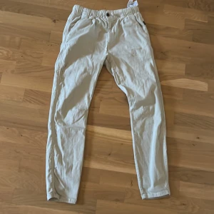 Beige chinos från Zara med resårmidja - Snygga beige chinos från Zara med elastisk midja och knappstängning. Byxorna har en klassisk rak passform och är tillverkade i ett mjukt bomullsmaterial. Perfekta för en stilren och avslappnad look. Säljer då jag inte använder dem.