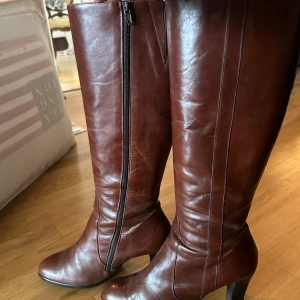 Bruna höga läderstövlar med klack - Säljer ett par snygga bruna stövlar i skinn med hög klack och dragkedja på sidan. Stövlarna  har bara använts runt 3 gånger och säljer dem just för att jag knappt använder dem. De är i otroligt bra skick och är gjorda av äkta läder. 