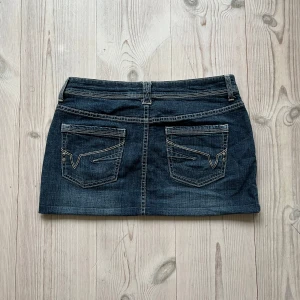 Blå lågmidjad jeanskjol  - Mörkblå lågmidjad jeanskjol från Yessica i fint skick. Kan inte hitta storlek men skulle säga S/M. Tvärs över midjan är det 40 cm och den är ca 30 cm lång. Använd gärna köp nu!
