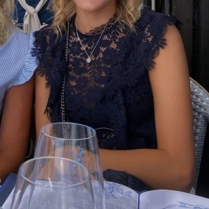  spetsblus med volangdetaljer från Zara - Säljer en marinblå blus i spets med vackra volangdetaljer vid axlarna. Blusen är ärmlös och har en rund halsringning. Perfekt för dig som vill ha en trendig och elegant topp till garderoben. storlek XS, från Zara