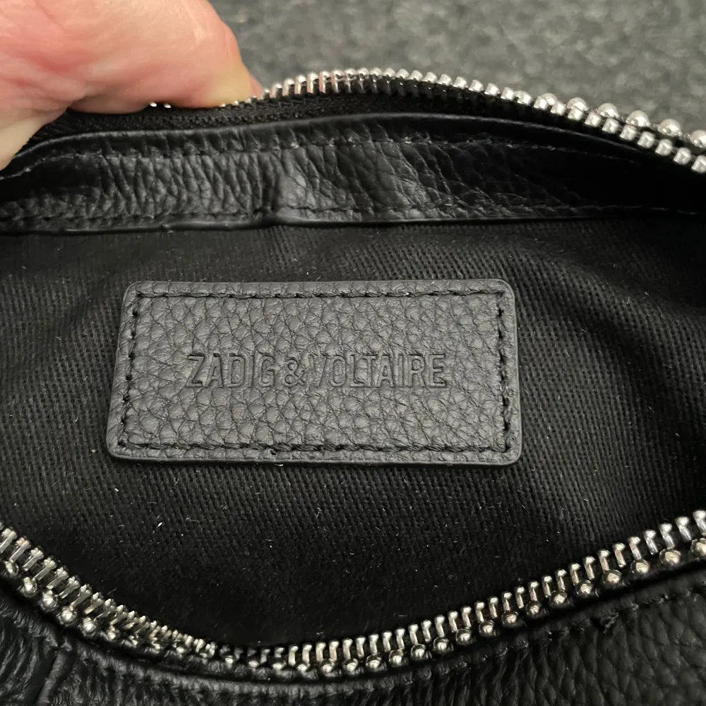 Svart handväska i skinn från Zadig & Voltaire. Modell: Sunny Logo Plaque XS Tote Bag. Den är i väldigt fint skick, använts ett fåtal gånger men mäst stått i garderoben. Har ett avtagbart axelband och kommer med original dustbag.😊. Laukut & Käsilaukut.