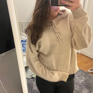 Beige stickad hoodie från Lindex - Mysig beige stickad hoodie från Lindex. Perfekt för kyliga dagar med sin mjuka och bekväma passform. Den har en justerbar huva med snören och långa ärmar. Ett måste för garderoben!