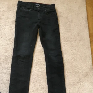 Svarta jeansbyxor från Tommy Hilfiger - Säljer ett par svarta jeansbyxor från Tommy Hilfiger med klassisk femficksdesign och diskret logga på myntfickan. Byxorna har normal passform och raka ben, perfekta till många olika outfits. Har typ 1-2 små fläckar som man kan se tydligare på bilden . 