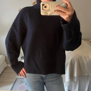 Mörkblå stickad polotröja - Mysig mörkblå stickad polotröja med lång ärm och hög krage. Tröjan har en avslappnad passform och breda ribbade muddar vid ärmslut och nederkant. Perfekt för kalla kvällar nu till sommaren!🍓