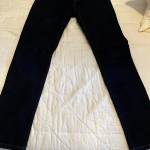 Mörkblå jeans från Filippa K - Säljer ett par klassiska mörkblå jeans från Filippa K, modell M. Rob i färgen indigo. Jeansen har raka ben, normal passform och traditionella fickor fram och bak. Perfekta för dig som gillar stilrena och tidlösa jeans.