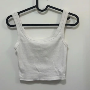 Vit croppad linnetopp - Säljer en enkel och stilren vit croppad linnetopp med breda axelband. Perfekt att matcha med jeans eller kjol för en avslappnad look.