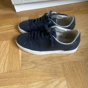 Mörkblå sneakers från ZARA - Säljer ett par mörkblå sneakers från ZARA med vita sulor och svarta skosnören. Skorna har en klassisk rund tå och platt sula, samt en enkel och stilren design. Perfekta för en avslappnad look.