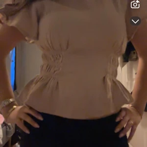 Beige blus med volang - Säljer en beige blus med korta ärmar och volang nertill. Blusen har insydda detaljer i midjan som ger en smickrande form och lätt struktur i tyget. Perfekt för dig som gillar en feminin och stilren look. Storlek m men tycker den sitter som s 