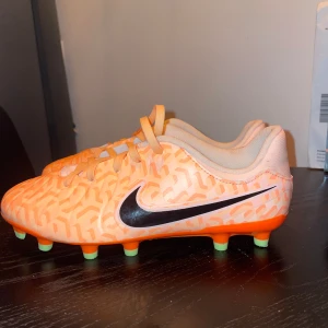 Nike tiempo legend 10 orange  - Säljer ett par i princip nya Nike fotbollsskor i en stark orange färg med ljusrosa och vita detaljer samt ett grafiskt mönster. Skorna har snörning, rund tå och gröna dobbar för bra grepp på planen. Perfekta för dig som vill sticka ut på fotbollsplanen! Använda vid max 5 tillfällen. Nypris ca 900. 