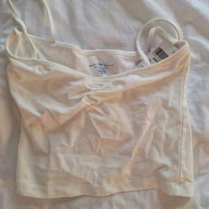 Topp från Brandy Melville - Säljer en vit croppad linnetopp från Brandy Melville med tunna axelband och lätt rynkdetalj framtill. Perfekt för varma sommar dagar och enkel att matcha med olika outfits. Prislapp kvar, nypris 176 🩷 Tror inte denna säljs längre. Passar XS-S. 