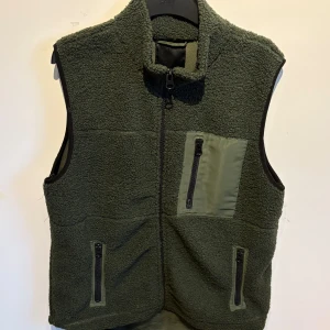 Grön fleeceväst - Mörkgrön fleeceväst från 157 med tre fickor med dragkedja, varav en bröstficka i kontrasterande material. Perfekt för lager-på-lager och håller dig varm under kyliga kvällar. Perfekt till sena sommar kvällar
