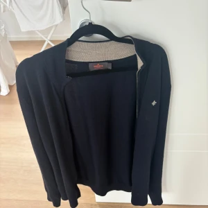 Svart kofta från Morris i merinoull - Säljer en svart kofta från Morris i 100% merinoull. Klassisk design med lång ärm och liten broderad logga på bröstet. Perfekt för lager-på-lager och passar till många olika stilar.