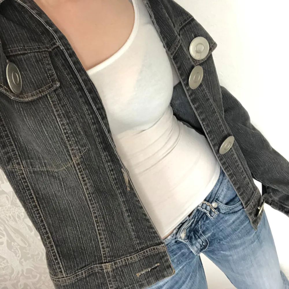 Cool svart jeansjacka med kontrastsömmar och stora, runda knappar framtill. Jackan har klassisk krage och långa ärmar. Perfekt för dig som vill ha en stilren men ändå unik look.. Takit.