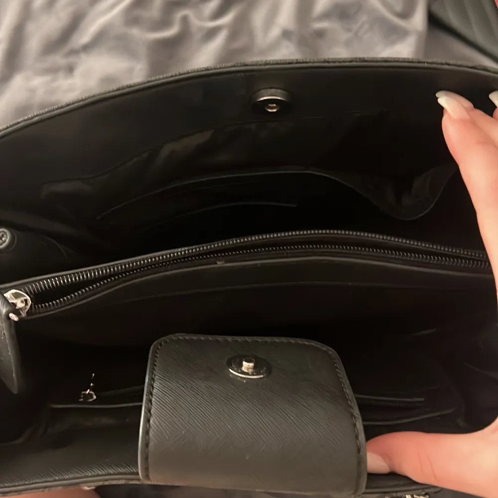 Säljer en svart axelväska från Guess med silverfärgad kedjerem och logotyp framtill. Väskan har präglat mönster med små G:n, flera fack inuti och stängs med magnetknapp. Perfekt för dig som vill ha en stilren och rymlig väska.. Laukut & Käsilaukut.