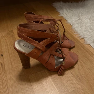 Bruna klackskor från Guess - Säljer ett par bruna klackskor från Guess med snygg snörning och tofsdetaljer framtill. Skorna har öppen tå och flätade detaljer längs kanterna. Perfekta för dig som vill sticka ut med en unik design. Inköpta på Sellpy men aldrig använda av mig 🩷