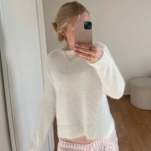 Vit fluffig stickad tröja - Mysig vit stickad tröja med fluffig känsla och rund halsringning. Tröjan har långa ärmar och breda ribbade muddar vid ärmslut och nederkant. Perfekt för lager-på-lager och en stilren look.