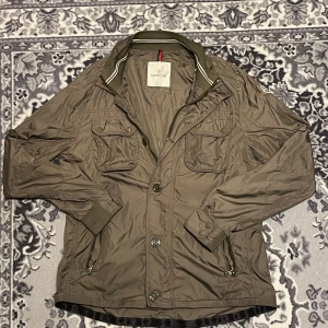 Moncler "Mate" field jacket - Säljer denna jätte fina moncler jacka i modellen mate, färgen är mörkgrön (ser ljusare och brunare ut på bilden). Jätte fint skick men saknar en knapp uppe vid halsen som absolut inte påverkar på något sätt då man aldrig har den helt knäppt. Storlek 3 som motsvarar ca S/M. Överlag jättefint skixk med mindre defekter.☺️såklart äkta och köpt på Second place i Malmö för ett rabatterat pris och har även kvittot. Kontakta vid bud/frågor.