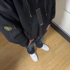 Stone island hoodie  - Säljer en svart hoodie från Stone Island med dragkedja och huva. Den har en ikonisk logga på ärmen och ribbade muddar. Perfekt för en casual look. 