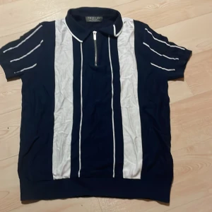 Mörkblå pikétröja med dragkedja - Säljer en stilren mörkblå pikétröja från Primark med vita ränder och dragkedja vid halsen. Tröjan har korta ärmar och en klassisk krage. Perfekt för en sportig look!