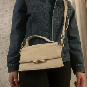 Beige axelväska med gulddetalj - Snygg beige axelväska, har några rå fläckar 