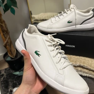 Vita sneakers från Lacoste - Snygga vita sneakers från Lacoste med klassisk design och gröna krokodilloggan på sidan. Skorna har snörning och en stilren look som passar perfekt till vardags. Tillverkade i syntetmaterial för en bekväm passform.