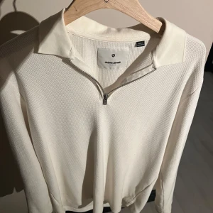 Vit tröja med dragkedja från Jack & Jones - Säljer en stilren vit tröja från Jack & Jones med dragkedja och krage. Tröjan har en enkel design och är perfekt för en avslappnad look. Passar bra till både jeans och chinos.