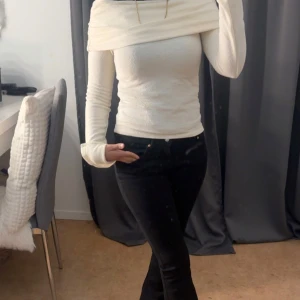 Vit långärmad tröja - Säljer en stilren vit långärmad tröja med en unik omlott-detalj vid halsen. Perfekt för en elegant look. Tröjan har en tight passform och är gjord i ett mjukt material.