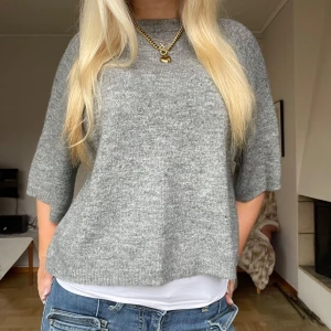 Grå stickad tröja - Säljer en stilren grå stickad tröja med trekvartsärm. Perfekt för en avslappnad look och enkel att matcha med olika outfits. Tröjan har en lös passform som ger en bekväm känsla.