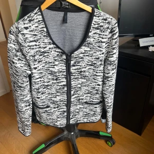 Svartvit mönstrad kofta från Imitz - Säljer en stilren svartvit mönstrad kofta från Imitz. Koftan har en rund halsringning och långa ärmar. Perfekt för att lägga till en touch av mönster till din outfit. Den har en dragkedja framtill och två fickor.