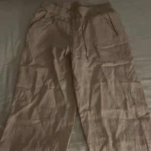 Beige byxor från Stories - Snygga beige linnebyxor från Stories i storlek S. Byxorna har en loose passform med elastisk midja. Byxorna är högmidjade men jag brukar vika ner dom för att få lågmidjade och det fungerar jättebra. Byxorna passar mig i längd som är 168💕