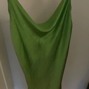 Grön klänning från Gina Tricot - Snygg grön klänning från Gina Tricot i ett glansigt material. Klänningen har en elegant drapering och är ärmlös, perfekt för en somrig look. Den har en avslappnad passform som ger en skön känsla.  Aldrig använt ! Den är i strl 42 men funkar lika bra som S-M