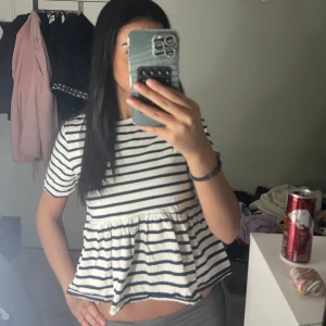 Randig topp från Zara - Säljer en söt randig topp från Zara i storlek S. Toppen har korta ärmar och en volangdetalj vid midjan som ger en fin siluett. Perfekt för en avslappnad stil med en touch av elegans. Säljer den för den används aldrig.