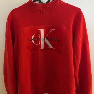 Röd tröja från Calvin Klein Jeans - Snygg röd tröja från Calvin Klein Jeans med deras ikoniska logga på bröstet. Tröjan har en klassisk rund hals och långa ärmar, perfekt för en stilren look. Passar bra till både jeans och kjol.