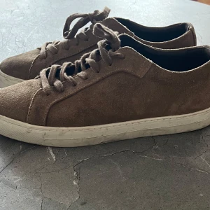 Bruna mockasneakers från Massimo Dutti - Snygga bruna sneakers i mocka från Massimo Dutti. De har en klassisk design med snörning och en vit sula som ger en stilren look. Perfekta för en avslappnad stil.